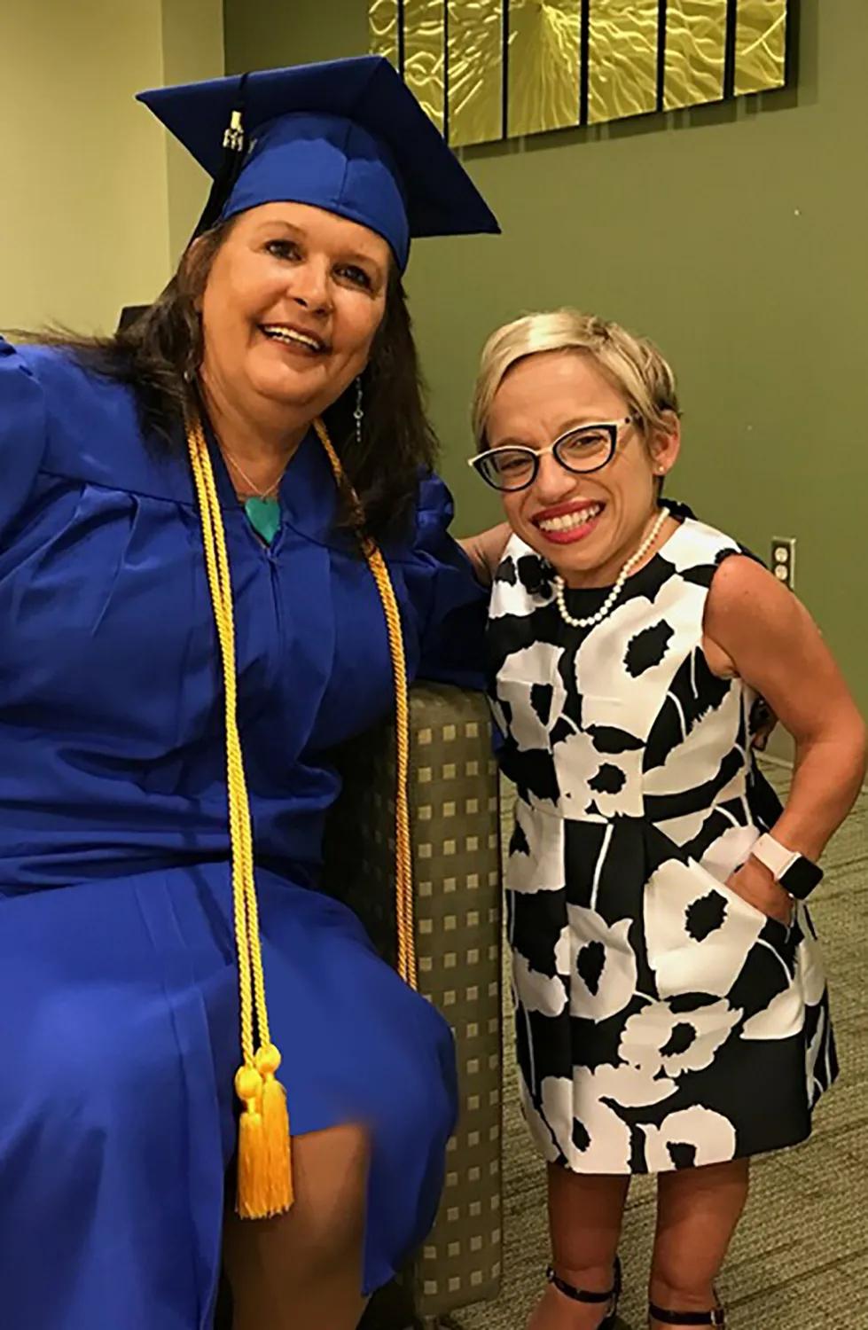 Debra Canady, dressed in a graduation robe and cap, smiles alongside Dr. Jennifer Arnold as they pose for a celebratory photo.