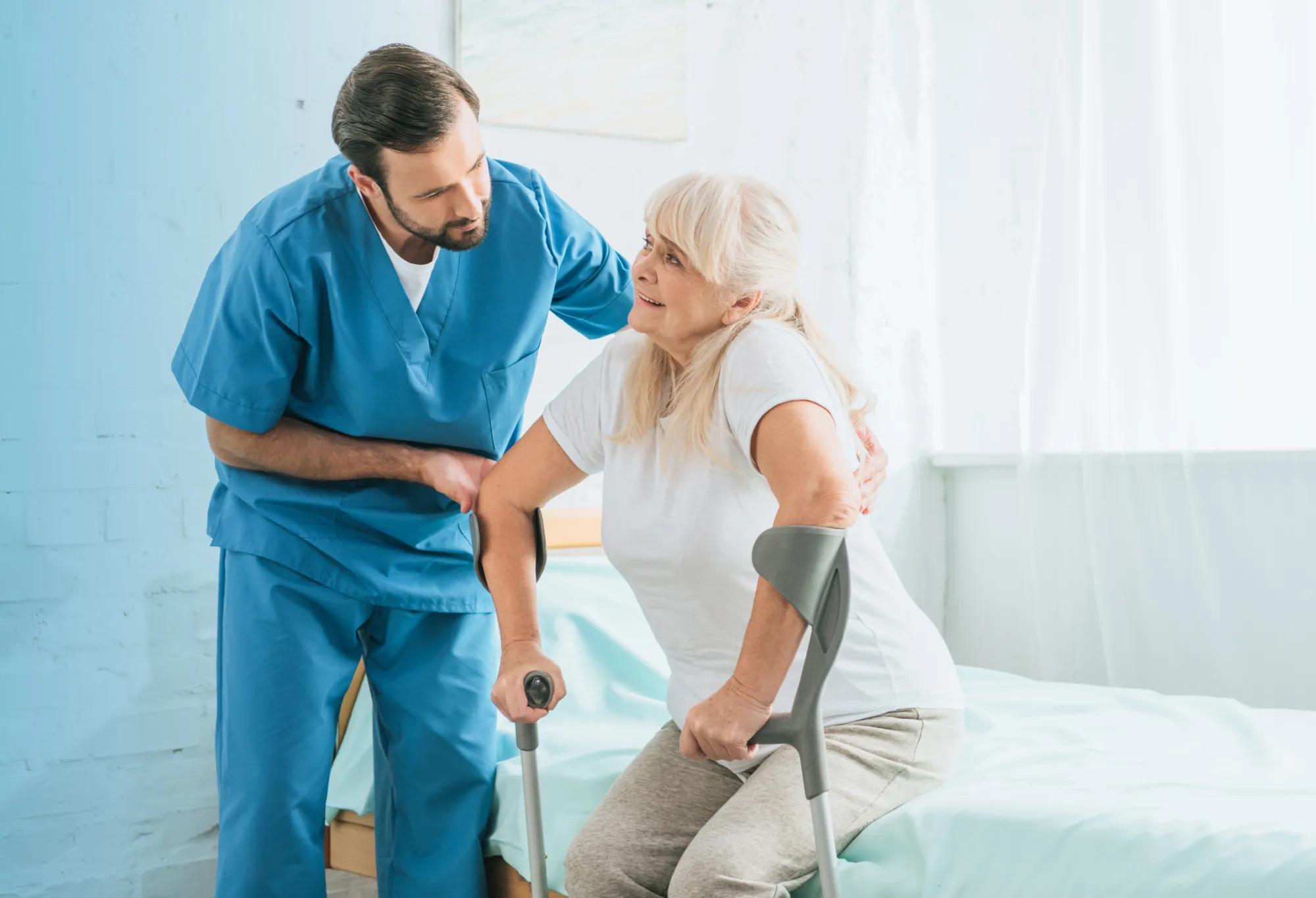 a patient care technician (PCT) helping a patient move from a hospital bed to a standing position