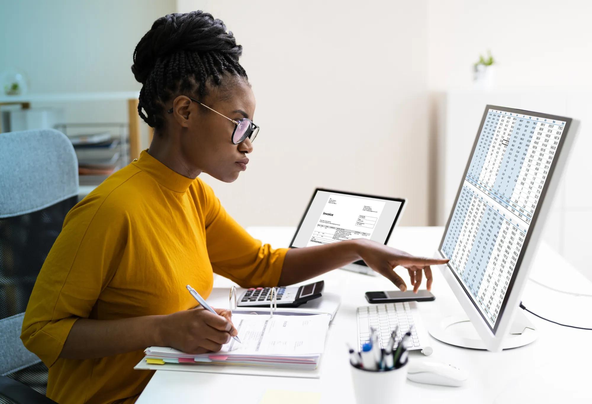A medical biller and coder using a calculator to tally a patient’s bill, which is on a computer screen