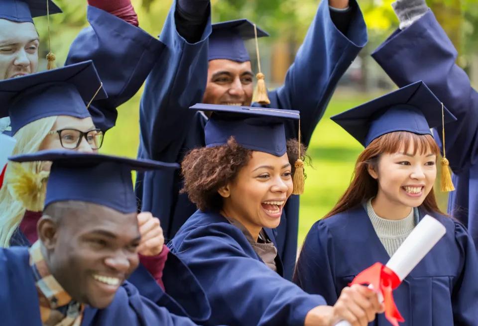 graduates raising their diplomas in the air to celebrate reaching their academic goals and finishing their healthcare programs