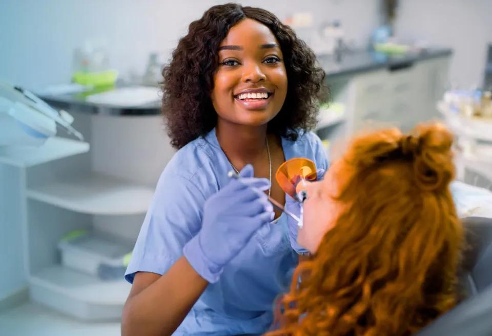 healthcare worker standing in a dental exam room and smiling after earning an associate degree in healthcare